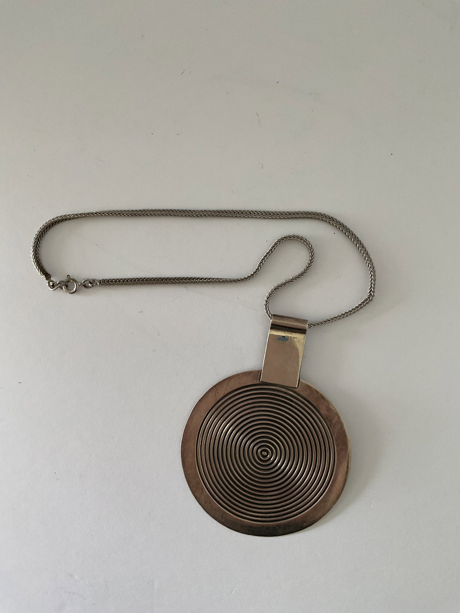 Mid Century Mexican Sterling Silver Statement Necklace: A mid century Mexican sterling silver statement necklace. The piece has an Art Deco feel with a circular disc design. It has a double herringbone chain that is 16" in length. The disc is 3" in