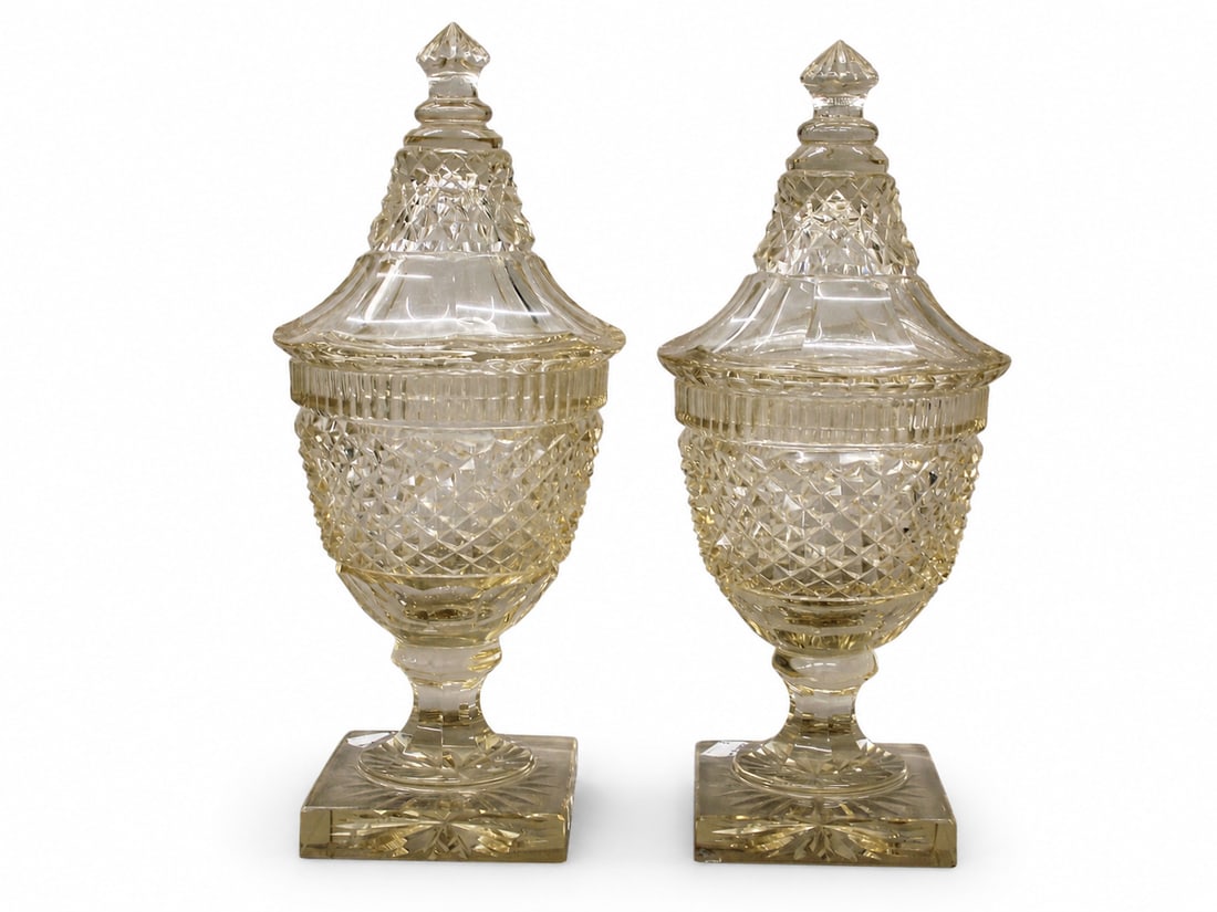 A pair of 19th century cut glass lidded vases: Dimensions: Height 31 cm. Description: A pair of 19th-century cut-glass lidded vases, possibly Irish. Each vase is formed with a faceted body, stepped foot and pointed cover, the cutting catching