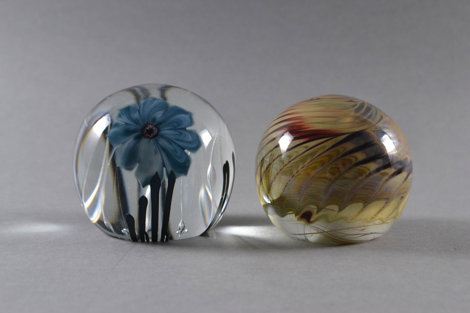 Josh Simpson (American), Two Early Art Glass Paperweights, 1980, 1984: One clear glass with blue flower, one with earth tone swirl designs, both signed Simpson, dated and numbered at base, H: 2 1/2"