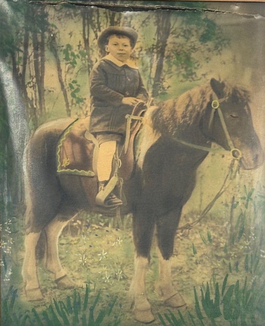 Antique Hand Tinted Photograph On Canvas Of A Young Boy On A Pony: taken in either Queens NY or Poland about 1900 Frame: 23 3/8 H x 19 3/8 W inchesCONDITION: Chips to edges of frame horizontal tear to top of image foxing and staining to verso of canvas