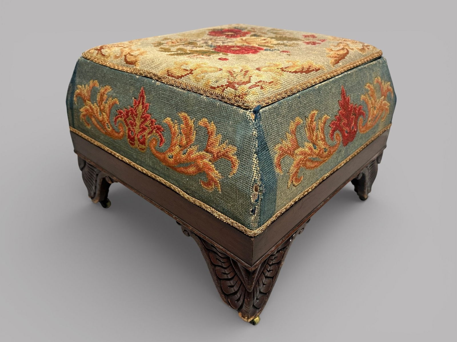 Victorian Footstool With Original Needlepoint Upholstery: the carved acanthus feet on casters the lid opens for storage h: 15 x w: 20 x d: 20 inches CONDITION: uphiolstery is worn from use and age hinges broken lining replaced finish loss scratches and dings