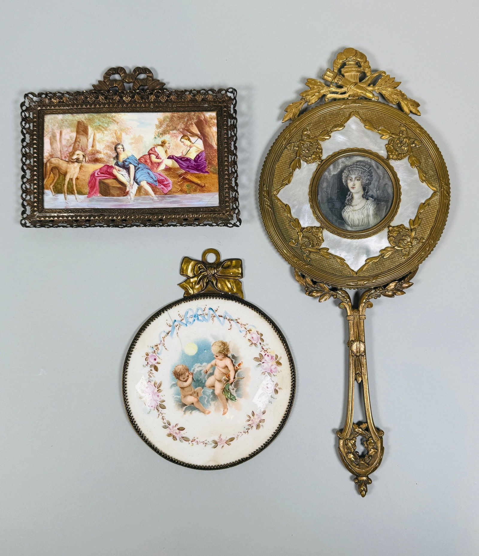 Palais Royal Gilt Metal, Mother-of-pearl And Enamel Hand Mirror: Together with two metal-framed figural enamels; mirror-H: 13 inches, putti enamel-H: 5 1/2 x w: 5 inches, bathing ladies-H: 5 x w: 6 1/2 inches