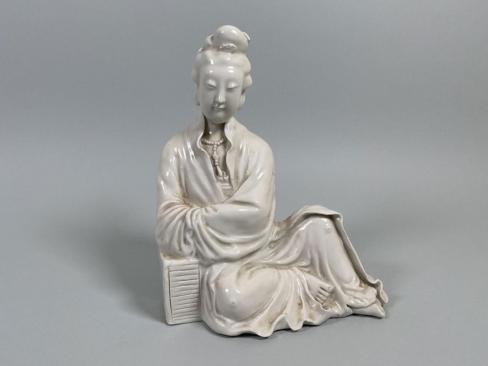 Blanc De Chine Porcelain Figurine Depicting Guanyin: impressed mark underneath h: 7 5/8 x w: 6 1/4 x d: 4 5/8 inches CONDITION: on small chip at figure’s knee