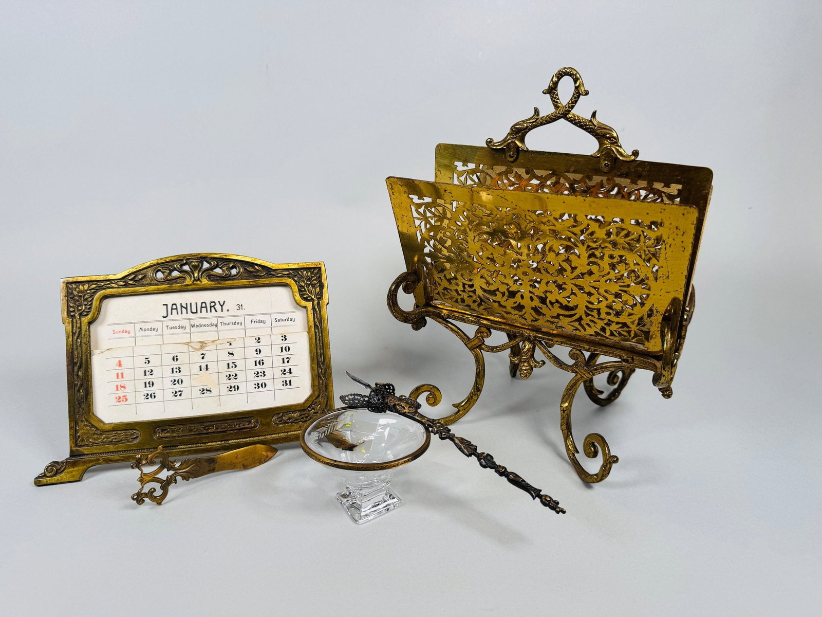 Collection Of Victorian Brass Desk Accessories, C. 1900 (4): includes an envelope opener h: 3 inches; a letter holder h: 9 x w: 7 x d: 6 inches; fountain pen and open ink pot h: 2 inches; art nouveau perpetual calendar h: 5 1/2 x w: 6 1/4 inches CONDITION: lett