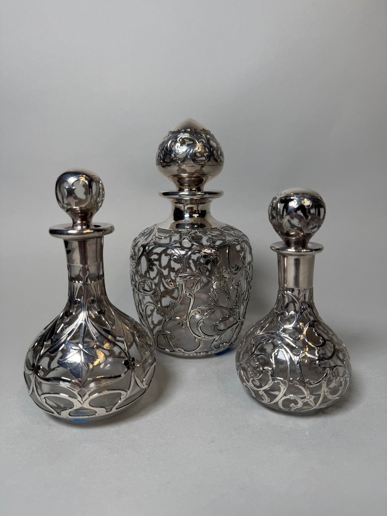 Three Gorham Fine Silver Overlay Scent And Vanity Bottles (3), C. 1900: The largest bottle having marks for Gorham/999/1000/Fine h: 6 x dia: 3 inches; smallest stamped Fine silver/999/1000 h: 4 x dia: 2 inches; the third bottle with Gorham marks h: 5 dia: 2 1/2 inches