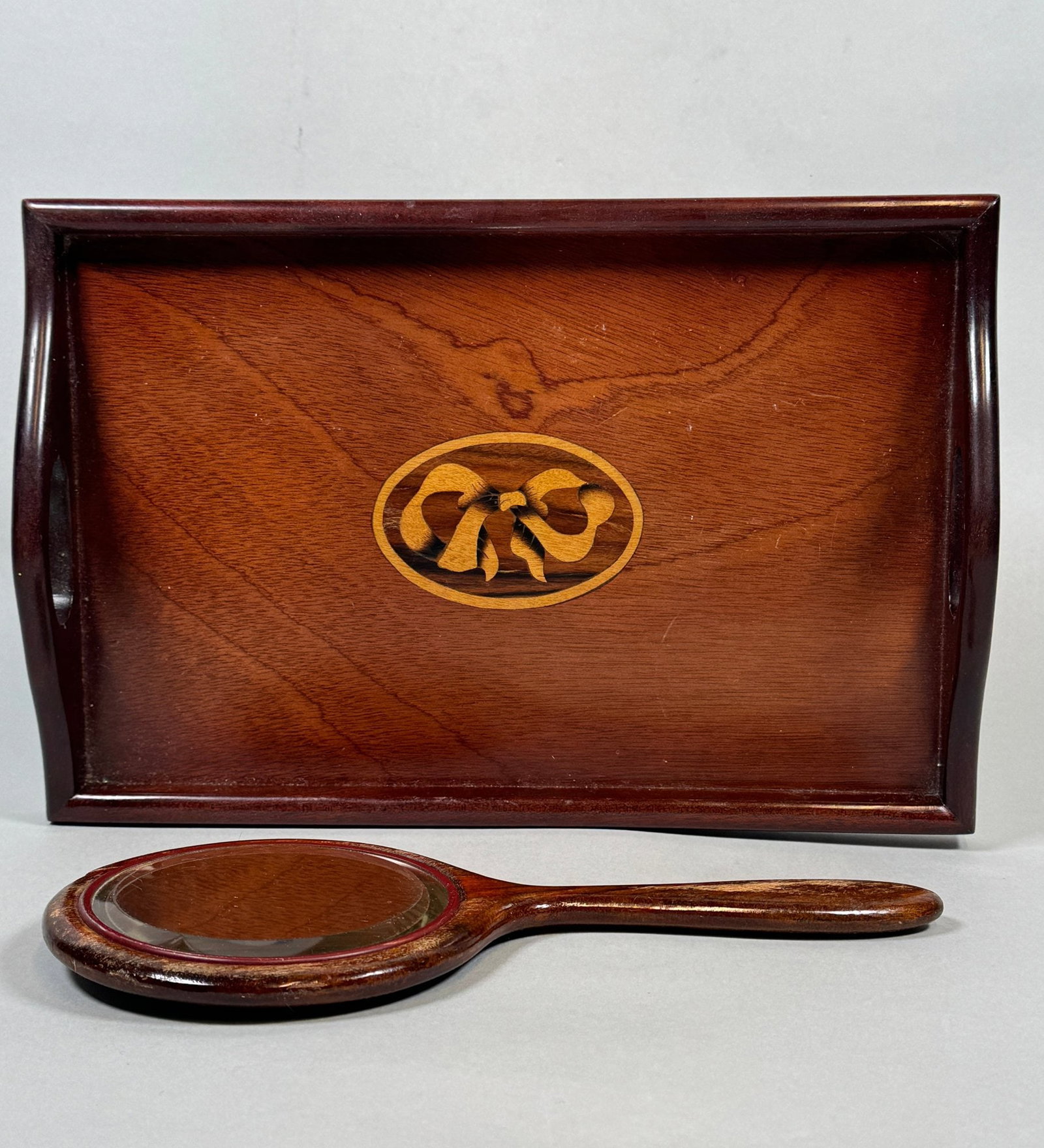 Vintage Manogany Vanity Tray And Sterling Silver Mounted Hand Mirror (2): Tray inset with marquetry ribbon bow w: 12 x d: 8 1/4 inches; the mirror medallion marked sterling at edge h: 10 inches CONDITION: worn finish on mirror