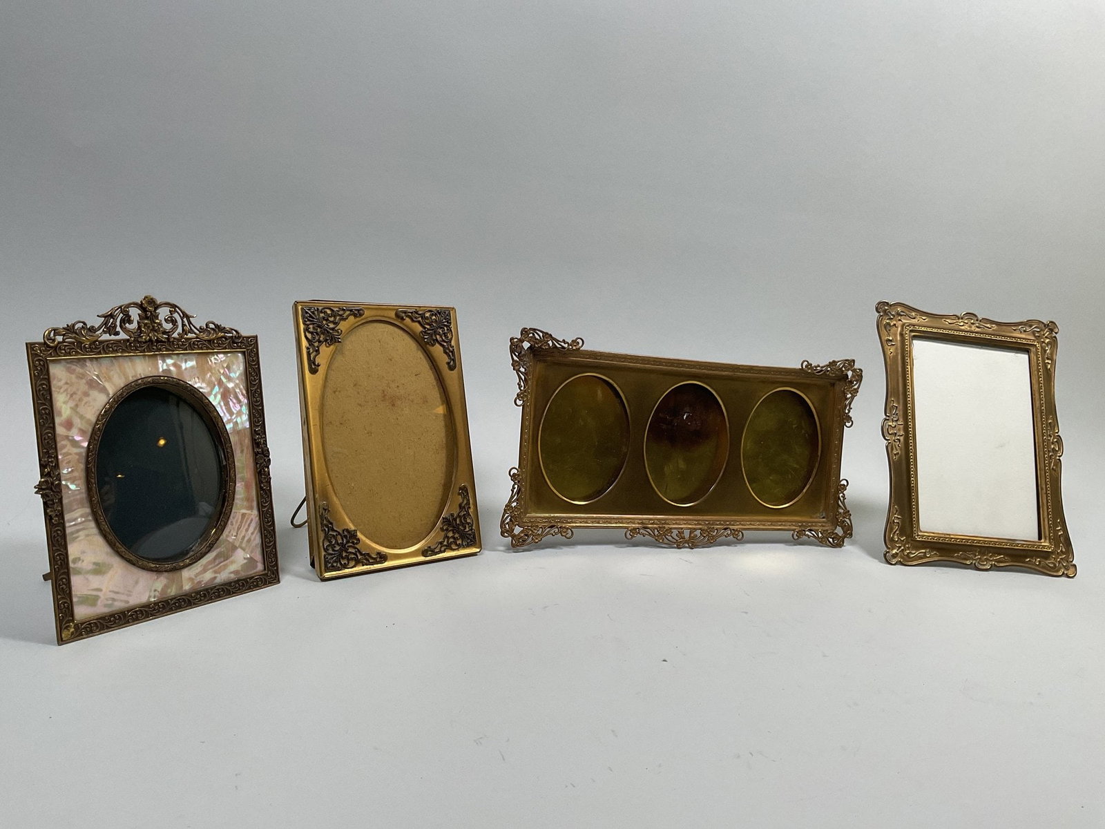 Collection Of French Gilt Brass Picture Frames, C. 1900 (4): the triple frame h: 5 1/8 x w: 10 1/4 inches (overall); mother-of-pearl with silk backing h: 5 5/8 x w: 4 1/4 inches (overall) CONDITION: gilding is worn with some scattered discoloration consistent w