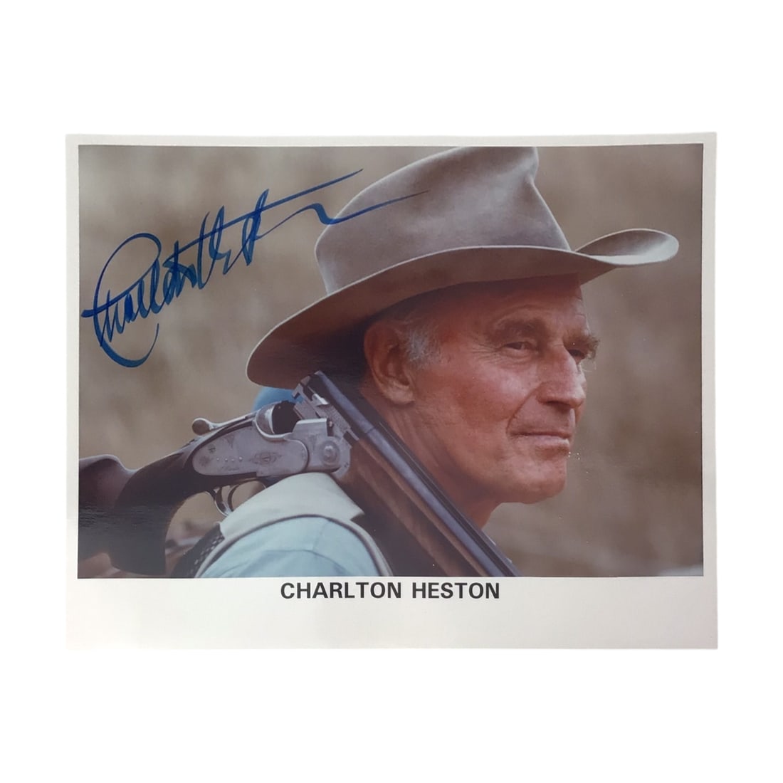 Charlton Heston Signed Photograph - Movie Entertainment Memorabilia: Here is a boldly signed color photograph of Charlton Heston, shown in a rugged pose with a shotgun. His autograph in blue ink runs clearly along the lower edge of the image, making this a strong candi
