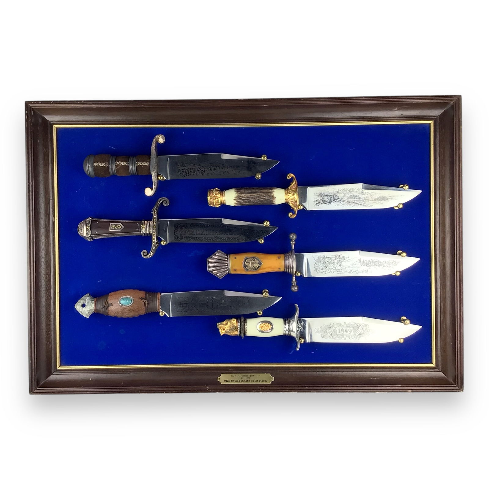 The Bowie Knife Collection Presented by The Western Heritage Museum: This impressive display features The Bowie Knife Collection as presented by The Western Heritage Museum, mounted in a hanging wooden frame and professionally matted in blue felt. The presentation meas