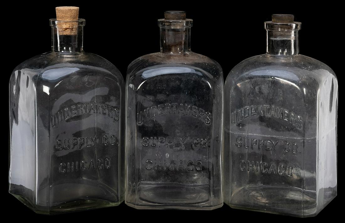 Undertakers Supply Co. Embalming Fluid Bottles. Three: Undertakers Supply Co. Embalming Fluid Bottles. Three clear glass 64 oz. bottles, embossed. Height 9 ¼”. Cork and rubber stoppers.