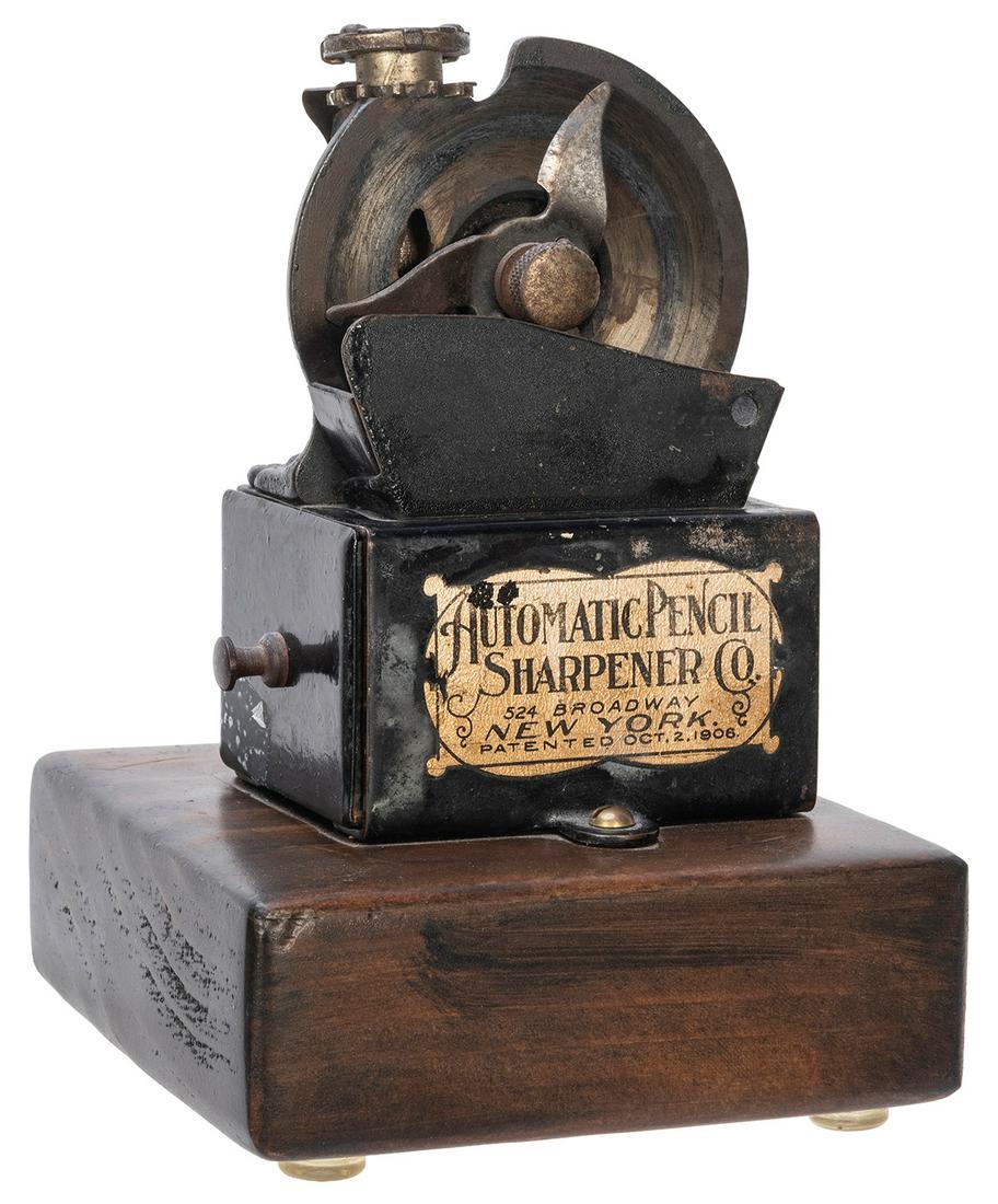 Automatic Pencil Sharpener. New York, pat. 1906. Sheet: Automatic Pencil Sharpener. New York, pat. 1906. Sheet metal and cast iron mounted on wooden base. With original label. Height 6”. Working.