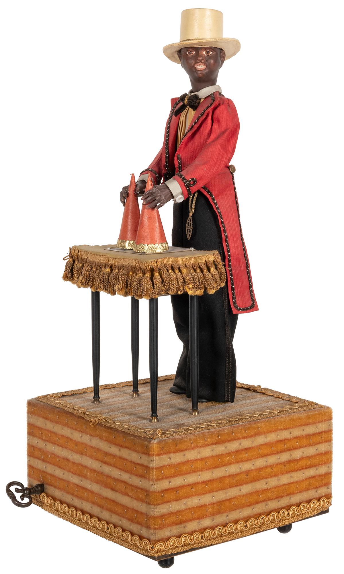 Minstrel Magician Automaton. France: Jean Farkas, ca.: Minstrel Magician Automaton. France: Jean Farkas, ca. 1960. Mid-century automaton of a black magician in a white top hat and red tails holding two cones over a table; as they are raised and lowered, t