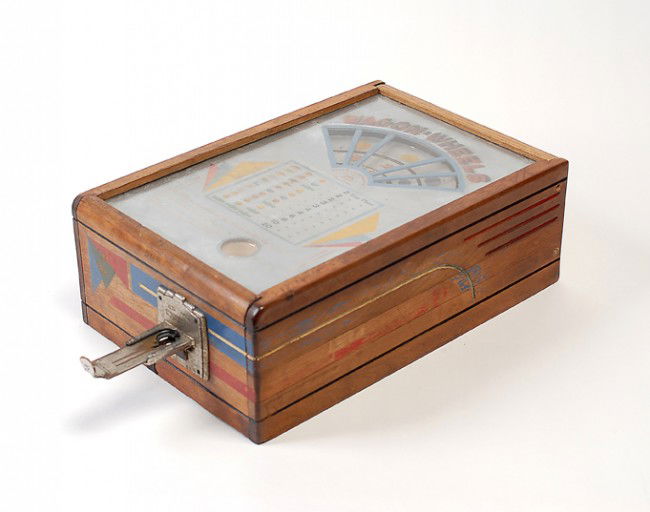 Wagon Wheels Twenty Five Cent countertop slot mach: Wagon Wheels Twenty Five Cent countertop slot machine. American, ca. 1935. Spring-driven mechanism spins internal wheel to determine payout. Wooden case with glass top measures 11 x 16 x 6". Fair cond