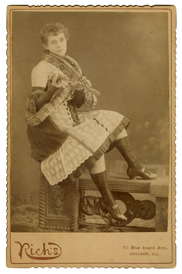 Cabinet photo of a snake charmer. Chicago: Rich’s, ca. 1900...: Cabinet photo of a snake charmer. Chicago: Rich’s, ca. 1900s/10s. Fine full-length photograph of the performer, seated and facing right, a serpent coiled around her neck and arms. Studio mount. 