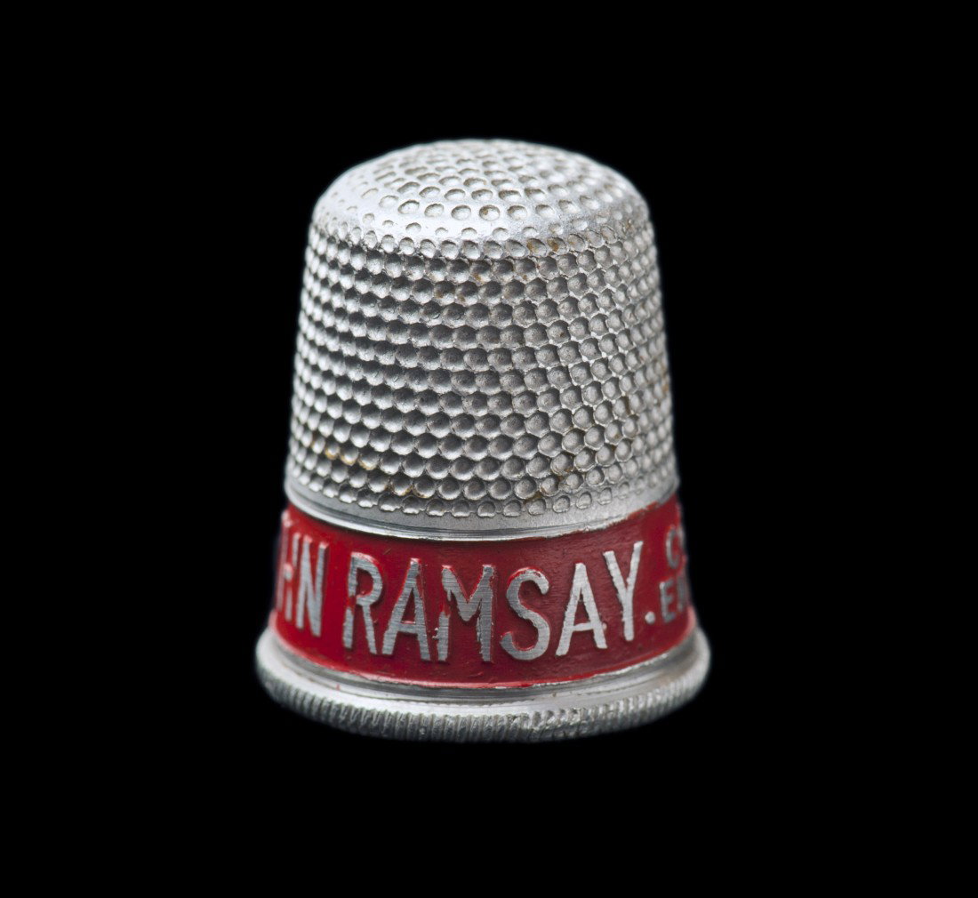 John Ramsay advertising thimble.: Ramsay, John. John Ramsay advertising thimble. Ayr Scotland, ca. 1950. Souvenir/advertising thimble with the text "John Ramsay Conjuring Entertainer Ayr" embossed in silver in a red enameled ring arou