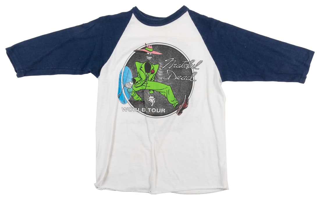 [GRATEFUL DEAD]. [SHELTON, Gilbert (b. 1940)]. Grateful Dea...: [GRATEFUL DEAD]. [SHELTON, Gilbert (b. 1940)]. Grateful Dead World Tour Ringer T-Shirt. Circa 1970s. Size large poly/cotton blue and white ringer shirt for the Grateful Dead World Tour. With Artwork o