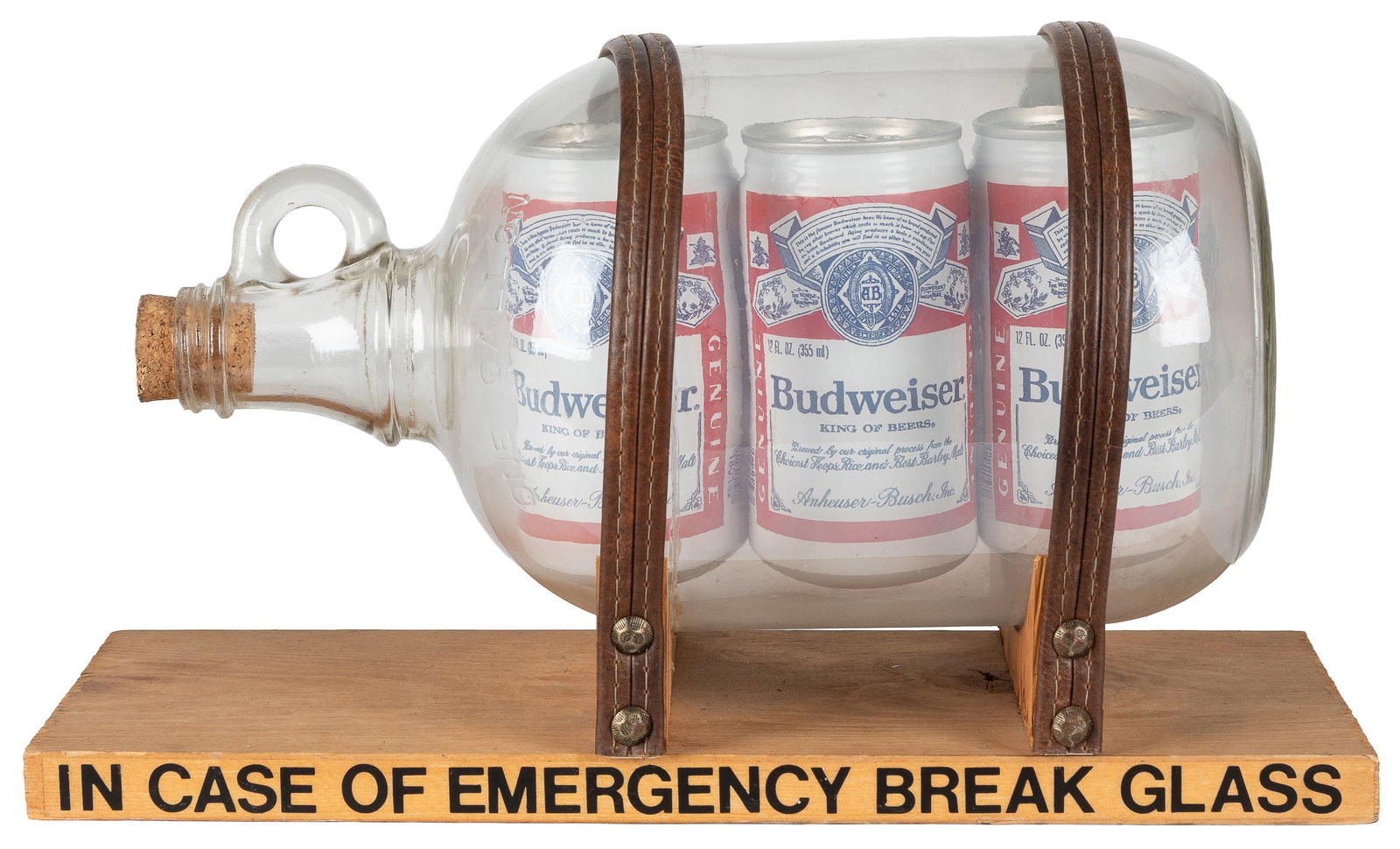 Budweiser "In Case of Emergency" novelty puzzle bottle.: Budweiser "In Case of Emergency" novelty puzzle bottle. Glass bottle sealed with cork, containing three cans of Budweiser. Held to wooden base with leather straps. 8 x 14 x 6".