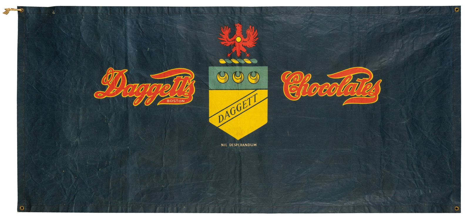 Daggett Chocolates Canvas Advertising Banner. Boston: Daggett Chocolate Company, ca. early 20th: Daggett Chocolates Canvas Advertising Banner. Boston: Daggett Chocolate Company, ca. early 20th century. Blue canvas banner featuring the chocolate company's script logo and shield emblem. 59 1/2 x 27