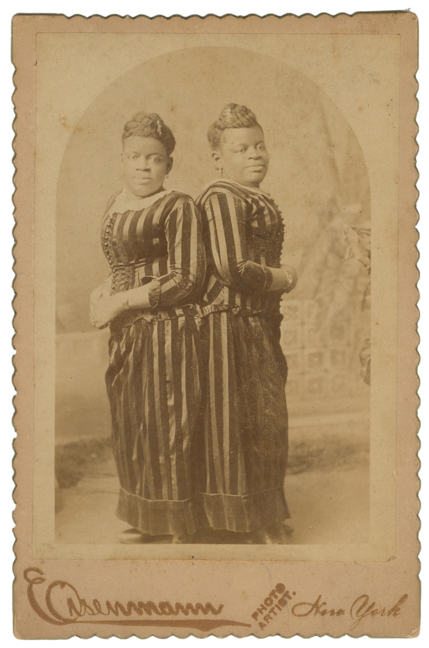 MILLIE-CHRISTINE (Millie and Christine McKoy, 1851-1912). Cabinet Card Portrait. Circa 1880s.: MILLIE-CHRISTINE (Millie and Christine McKoy, 1851-1912). Cabinet Card Portrait. New York: Eisenmann, ca. 1880s. Cardstock mount with scalloped edges. Full-length portrait of the conjoined twins, also