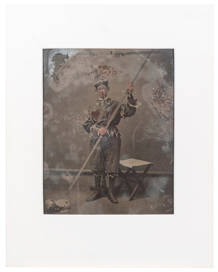 [EARLY PHOTOGRAPHY]. Whole-plate Tintype Photograph of a Circus Clown. Circa 1860s/70s.: [EARLY PHOTOGRAPHY]. Whole-plate Tintype Photograph of a Circus Clown. Circa 1860s/70s. Striking full-length image with hand-tinting, depicting a young male performer holding a long pole diagonally in