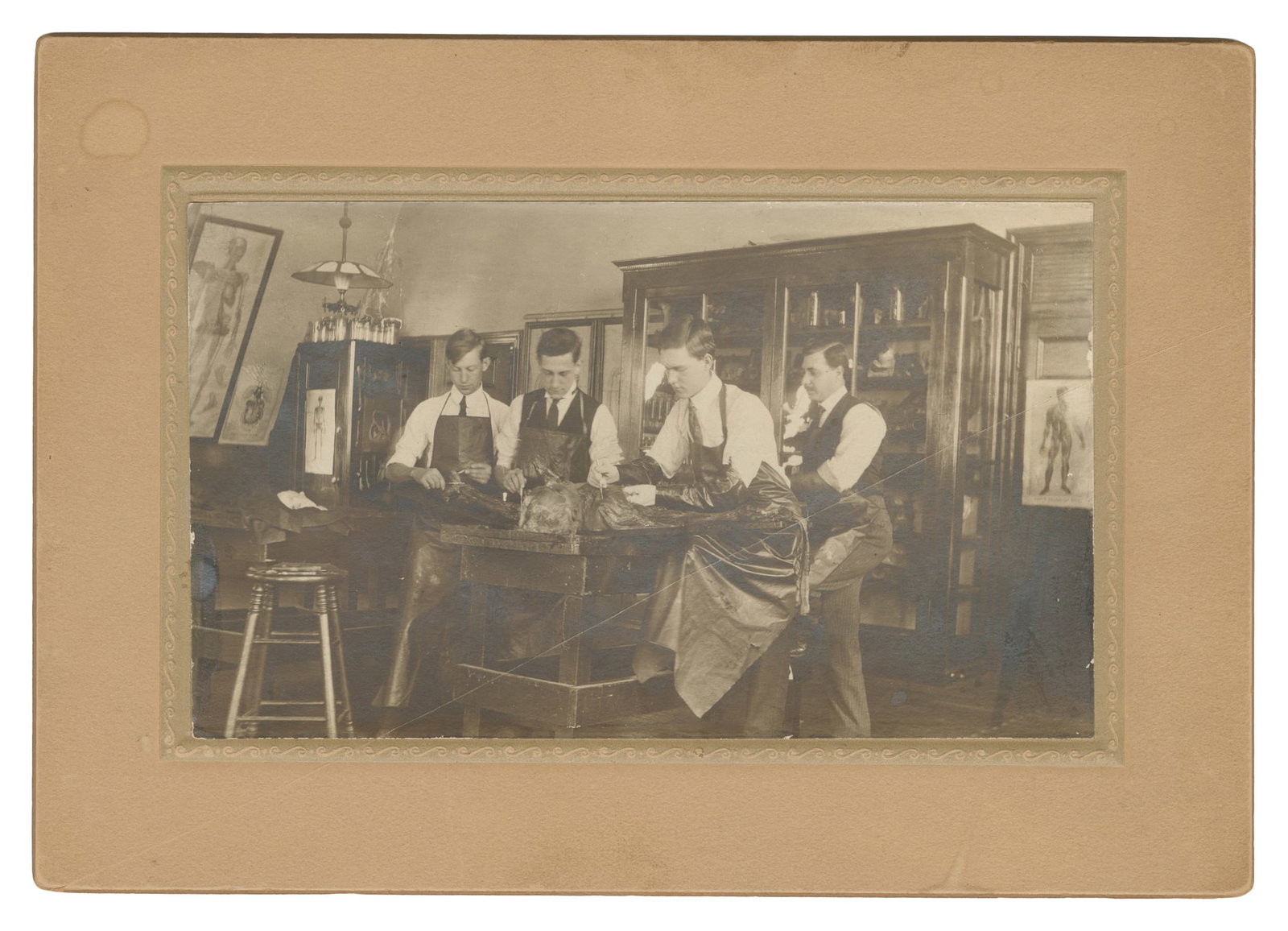 Mounted Anatomical Dissection Photograph. 1908-09.: Mounted Anatomical Dissection Photograph. 1908-09. Photograph on decorative mount, dated and inscribed with the students' names on verso. Depicts 4 students working on a cadaver in an anatomy