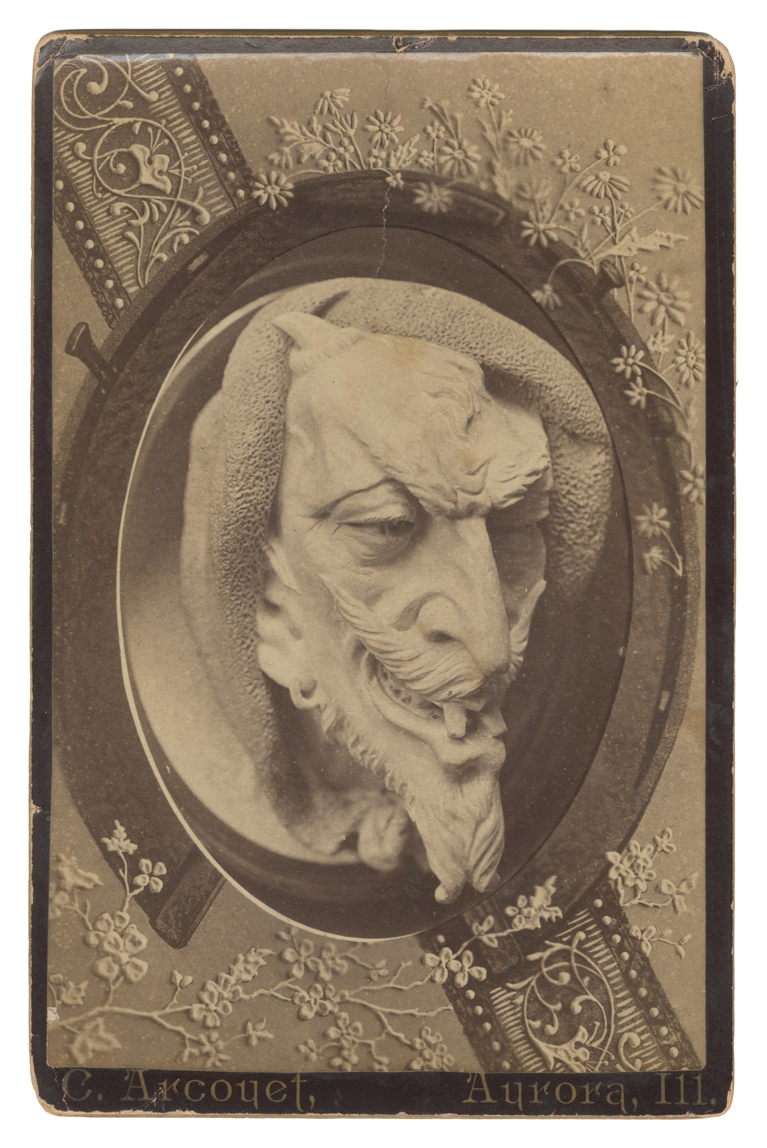 Cabinet Card of Satan. Aurora, IL: C. Arcouet, late 19th century.: Cabinet Card of Satan. Aurora, IL: C. Arcouet, late 19th century. Oval portrait of the devil's head with a goatee, prominent mustache, hooked nose, and small horn peeking out of a hood. 6 1/2 x 4