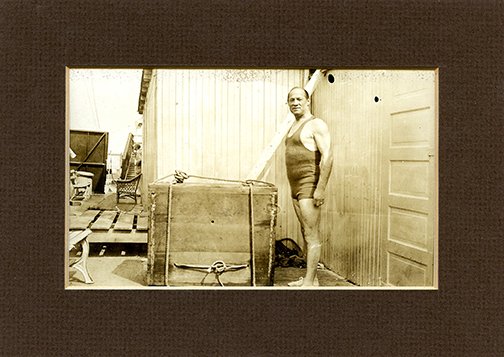 Photograph of Hardeen and the overboard packing box.: Hardeen. Photograph of Hardeen and the overboard packing box. Circa 1940. Full-length candid photograph shows Houdini’s brother standing next to a wooden packing case from which he would escape afte