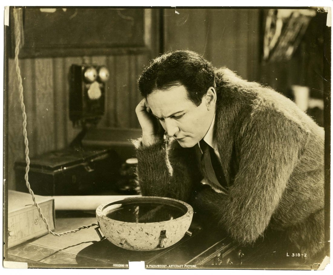 Houdini, Harry. Movie Still of Houdini in Terror: Houdini, Harry. Movie Still of Houdini in Terror Island. Los Angeles, [1920]. Sepia tone proof photo depicting Houdini wearing mohair sweater while looking through periscope. Serial No. L 318-2. Margi