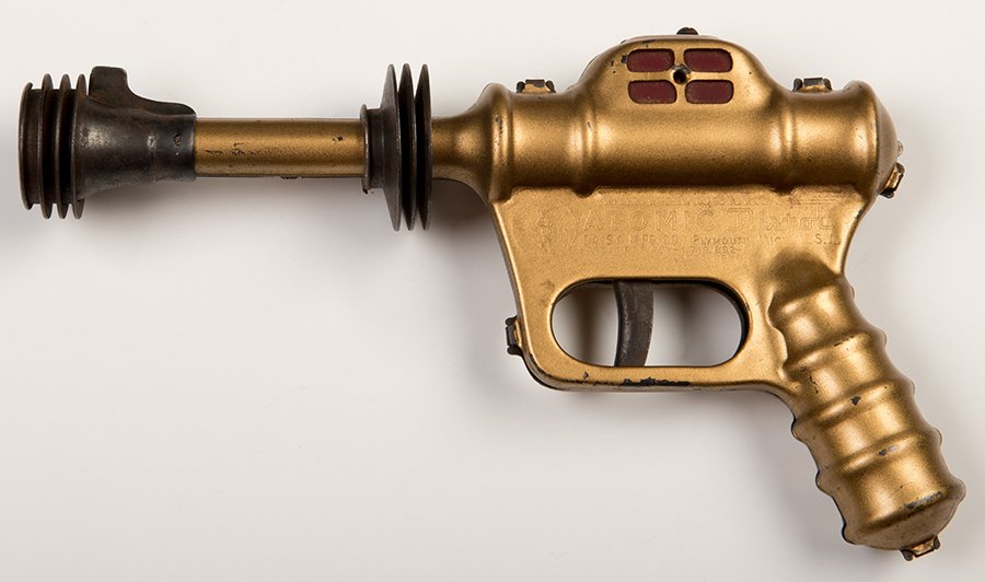 Buck Rogers U-235 Atomic Pistol. Plymouth, Mich.: Daisy: Buck Rogers U-235 Atomic Pistol. Plymouth, Mich.: Daisy Manufacturing, ca. 1940s. Gold-tone finish version of this metal toy gun from the Buck Rogers franchise. 10 long. Some oxidation on exposed meta