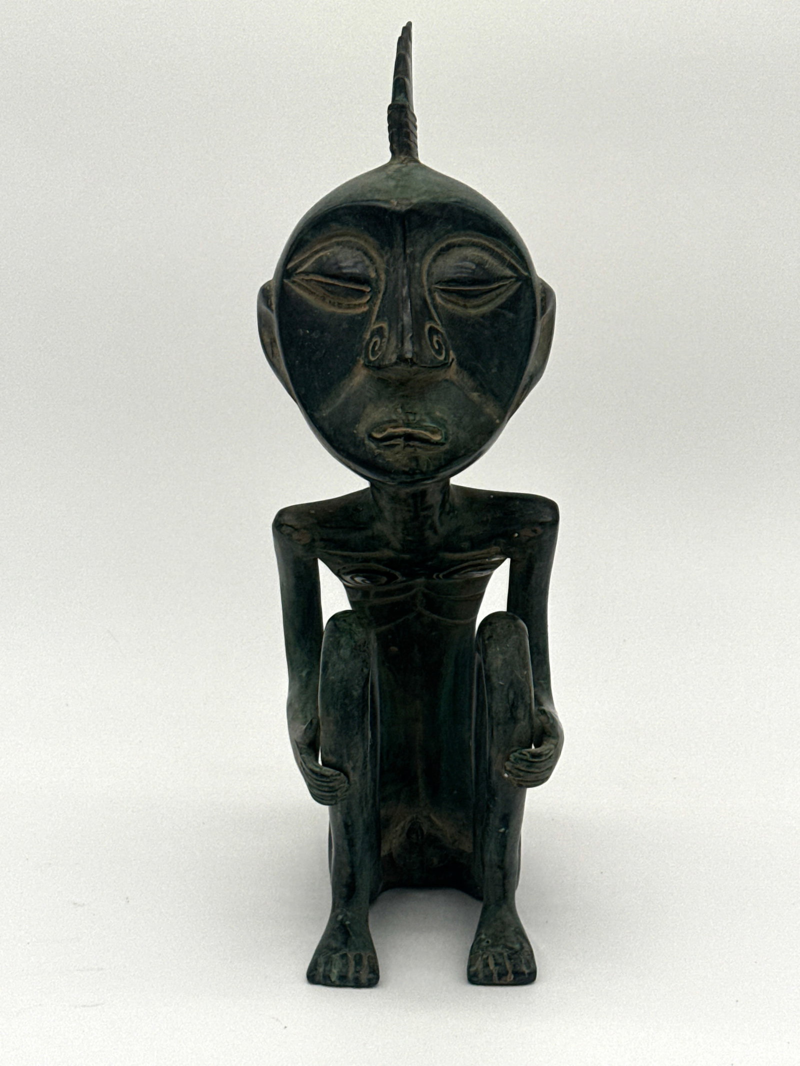 Cast Metal Stylized Ancestor Figure with Lizard Motif 4" x 13" x 5.5": "This solid cast metal figure, standing 13 inches tall, is a highly stylized anthropomorphic form seated in a crouched position. The exaggerated features—elongated limbs, pronounced facial mask with