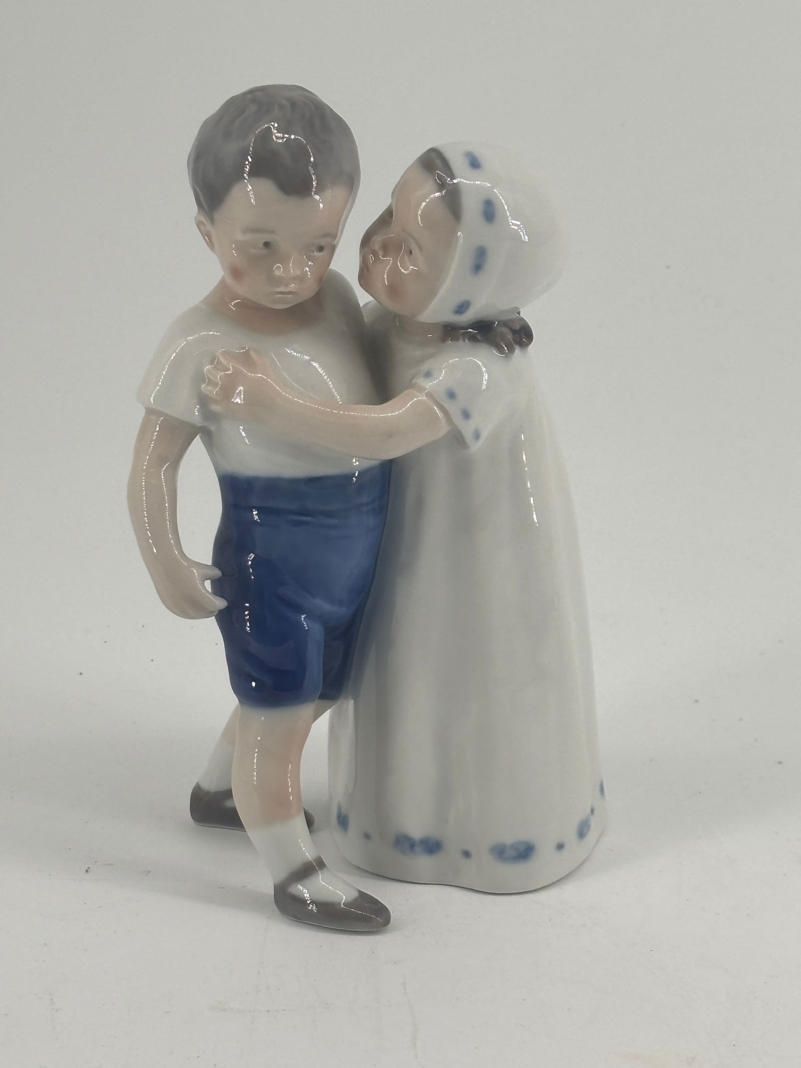 Copenhagen Porcelain Boy & Girl Figurine – 4x3x7 in.: Tender figurine of a boy and girl seated together, rendered in soft blue-gray and ivory glazes. Naturalistic modeling and gentle expressions showcase Scandinavian porcelain craftsmanship. A serene dec
