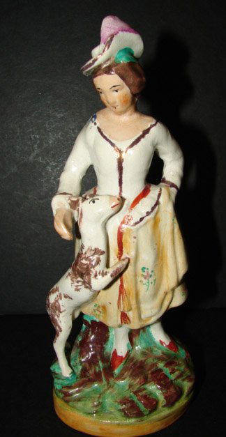 STAFFORDSHIRE FIGURINE: STAFFORDSHIRE FIGURINE. Depicts a Colonial female with dog. Shows crazing throughout. Marked on bottom "Old Staffordshire/Wade/England". 7.25" H.
