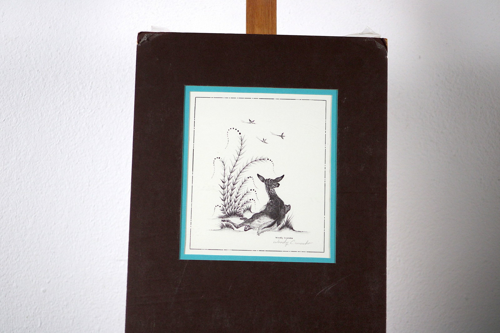 Woody Crumbo Deer Pencil-Signed Print: Woody Crumbo (Potawatomi, 1912-1989), "Deer." Black-and-white line print depicting a single deer reclining on the ground with legs tucked beneath it, head raised and gazing upward toward three birds i