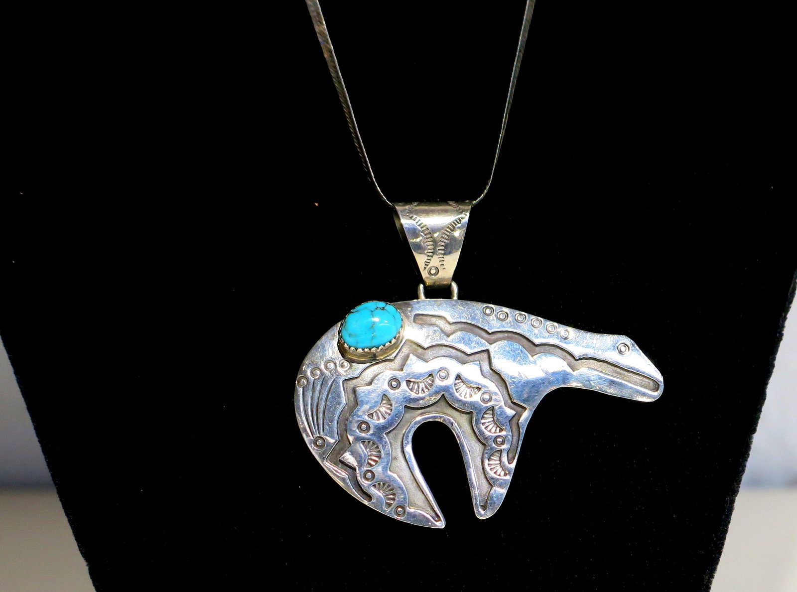 Navajo Sterling Bear Pendant with Turquoise: Navajo sterling silver bear pendant, cut in a stylized standing profile with an arched heartline back, notched paw, and open negative-space leg. The surface is worked in fine traditional stampwork - s