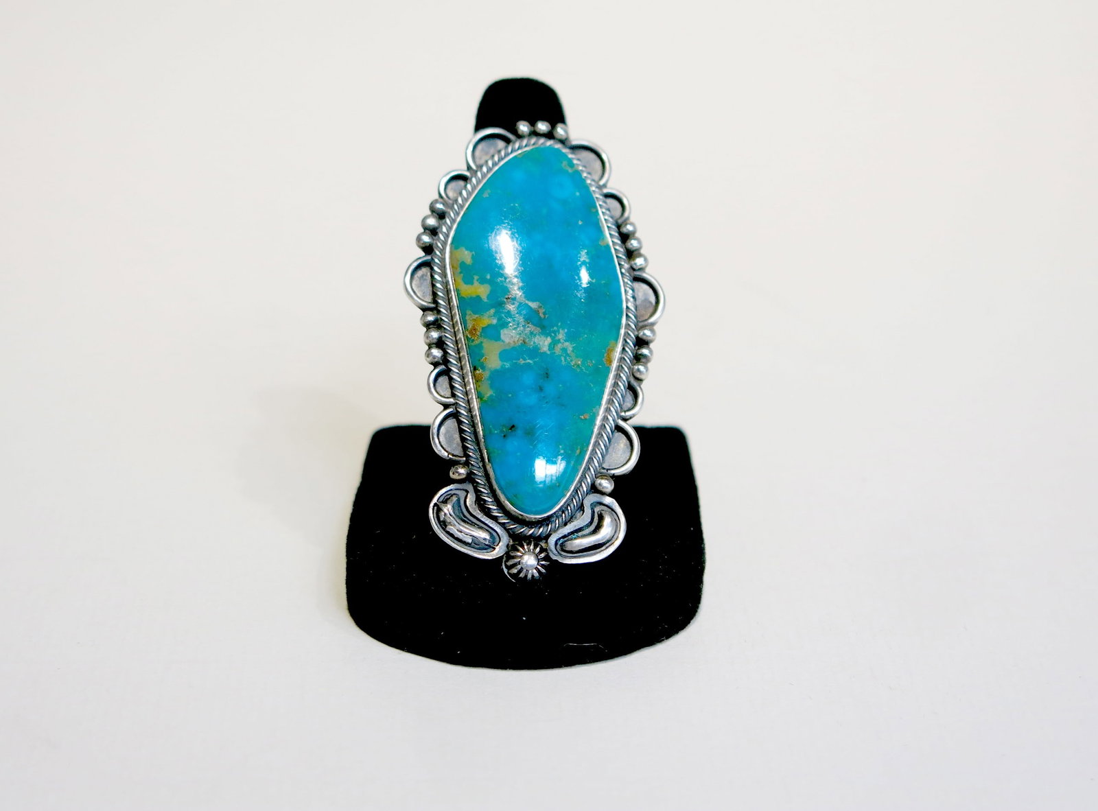 Navajo Sterling Large Turquoise Statement Ring: Blue-green turquoise with golden-brown matrix, possibly Royston or Kingman. The setting features a twisted rope wire bezel, flanked by hand-applied silver shot in a scalloped arrangement, with elabora