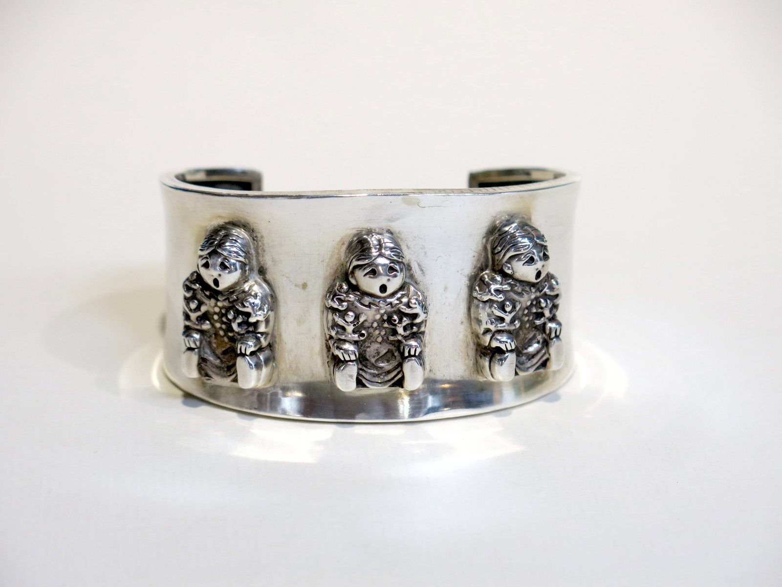Navajo Sterling Three-Figure Storyteller Cuff: A wide, heavy-gauge sterling silver storyteller cuff bracelet featuring three identical cast or fabricated figures applied in high relief to a polished smooth band. Three-figure storyteller cuffs of t