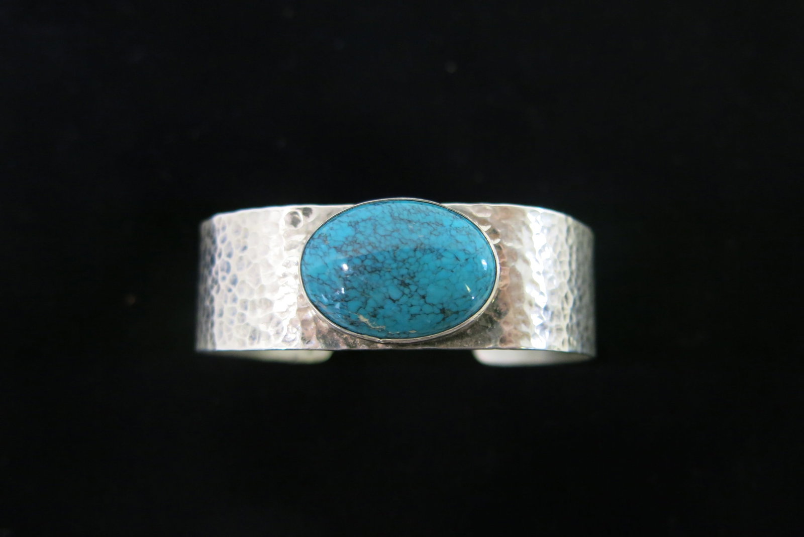 Navajo Hammered Sterling Turquoise Cuff Bracelet: A wide sterling silver cuff bracelet with an all-over hand-hammered/planished textured finish, set with a single large oval turquoise cabochon in a smooth silver bezel. The turquoise displays a light-