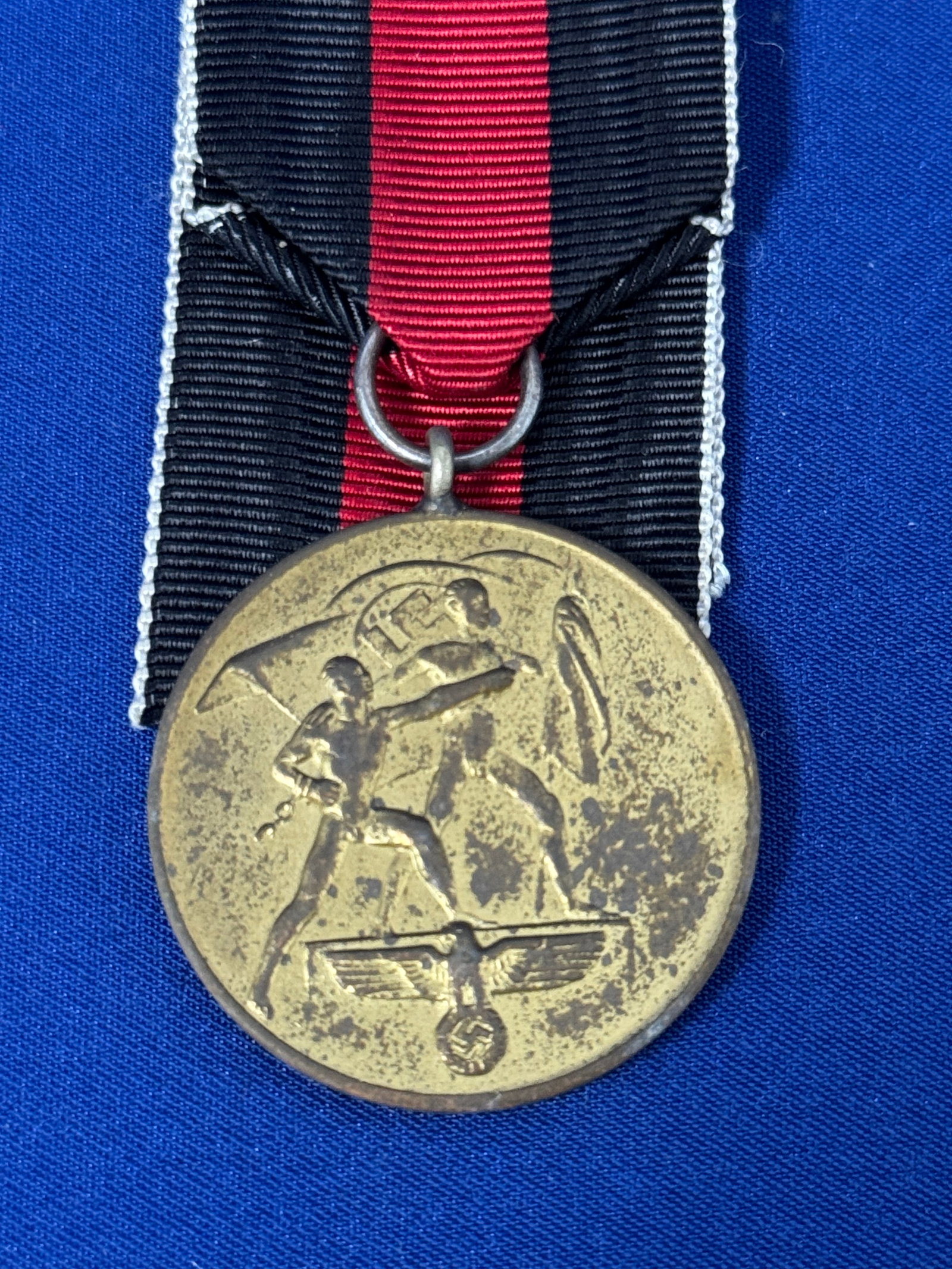 WW2 German Sudentland Medal with Ribbon: WW2 German Sudentland Medal with RibbonA circular medal constructed of bronze, the obverse bears two nude male figures, one of which holds a flag with a swastika that flies behind them, both are stand