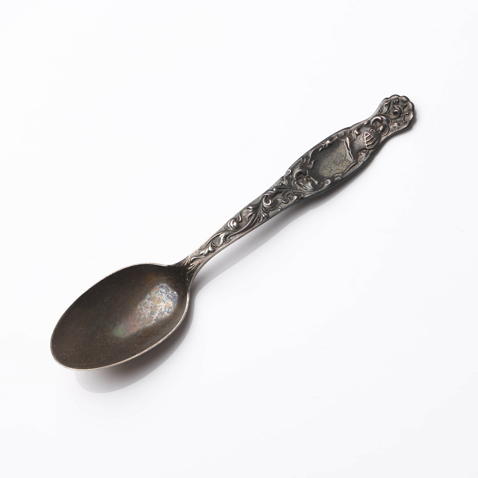 A STERLING SILVER REPOUSSÉ TEASPOON, EARLY 20TH CENTURY: Dimensions Length: 5 15/16 in (15.1 cm); Weight: 30.7 g Description: This early 20th-century sterling silver teaspoon features an ornate repoussé handle decorated with scrolling foliage and shield-sh