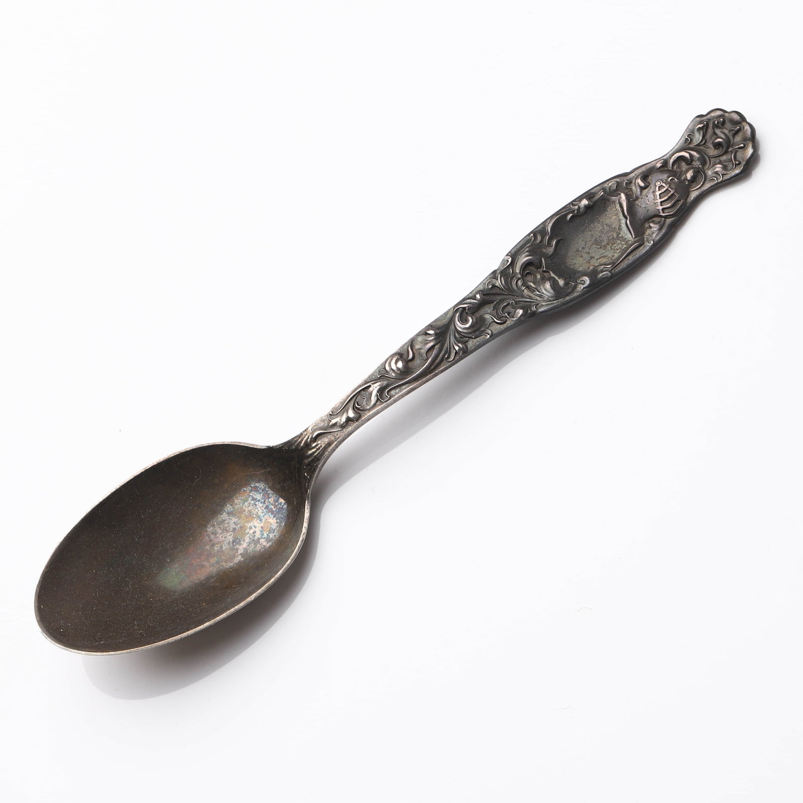 A STERLING SILVER REPOUSSÉ TEASPOON, EARLY 20TH CENTURY: Dimensions Length: 5 15/16 in (15.1 cm); Weight: 30.7 g Description: This early 20th-century sterling silver teaspoon features an ornate repoussé handle decorated with scrolling foliage and shield-sh
