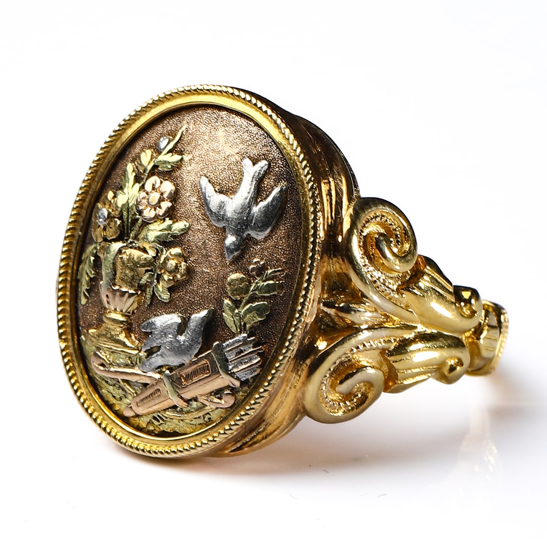 VICTORIAN 18K GOLD MULTI-COLOR GOLD BIRD AND FLOWER RING: Dimensions Ring size approx. 7 1/2 (inner diameter 11/16 in. / 18.7 mm)Weight: 11.2 g Description A Victorian 18K gold ring featuring an oval plaque decorated in polychrome gold with an applied