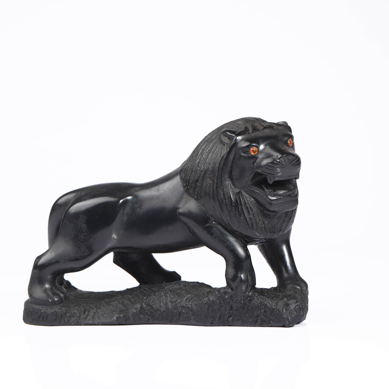 A BLACK STONE CARVED LION FIGURE: Dimensions Length: 7 5/16 in (18.5 cm); Height: 5 1/8 in (13 cm) Description ?This black stone lion figure is carved in a powerful striding pose, its muscular body contrasted with a deeply incised
