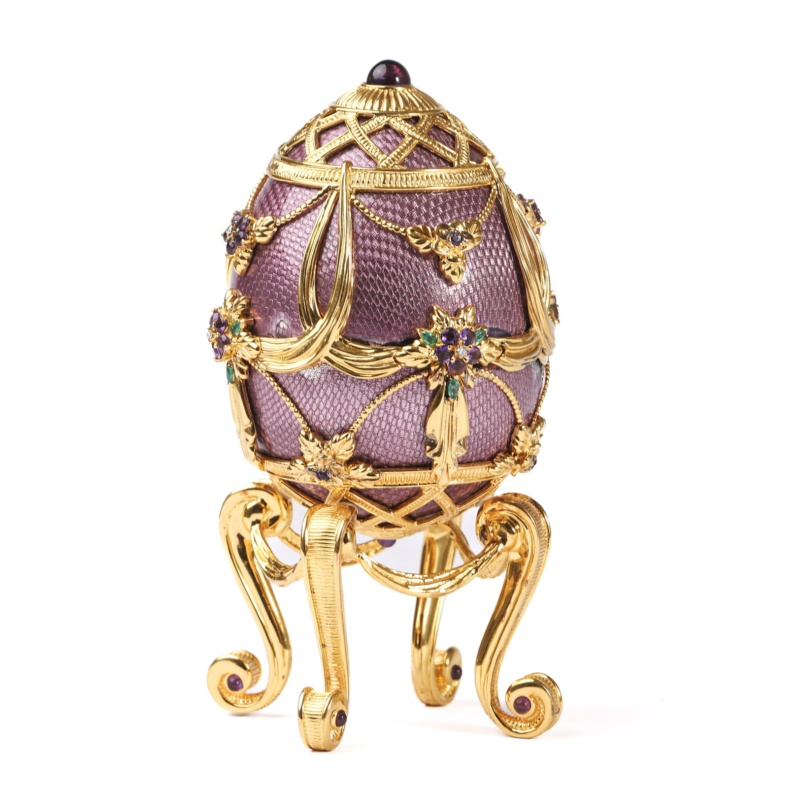 A HOUSE OF FABERGÉ COMMEMORATIVE EGG, LATE 20TH CENTURY: Dimensions Height 5 1/2 in (14 cm) overall with stand; Egg height 4 1/8 in (10.5 cm); Diameter 3 in (7.5 cm). Description: The ovoid form in lilac guilloché enamel, richly mounted in gilt .925