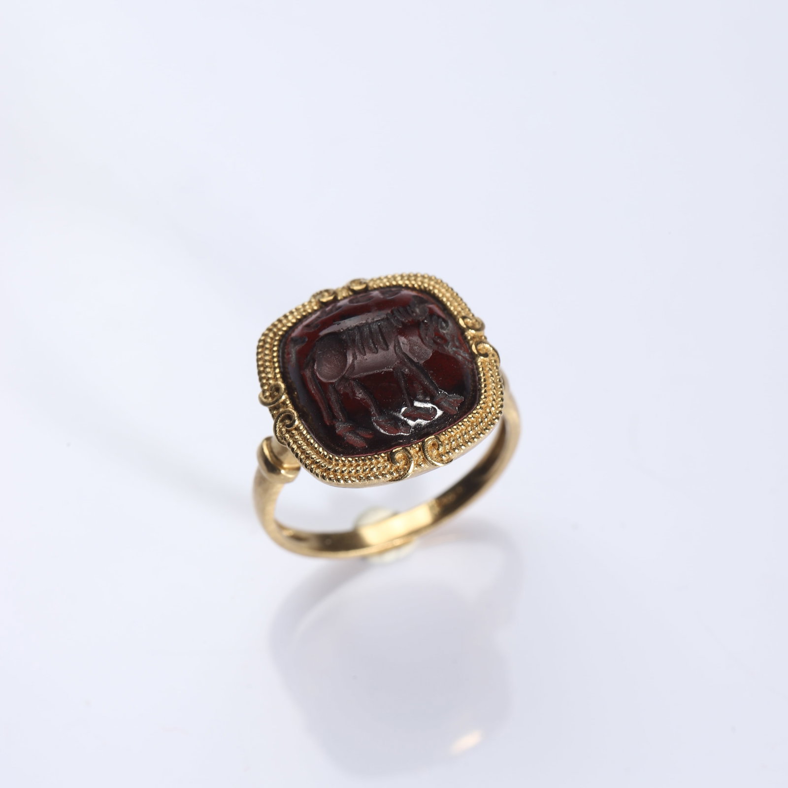 AN ANCIENT INTAGLIO GARNET GOLD RING: Dimensions Inner diameter: 21/32 in (16.7 mm); Weight: 5.7 g. Description A refined ring set with an ancient dark red garnet intaglio, engraved with a quadruped animal rendered in a stylized classical