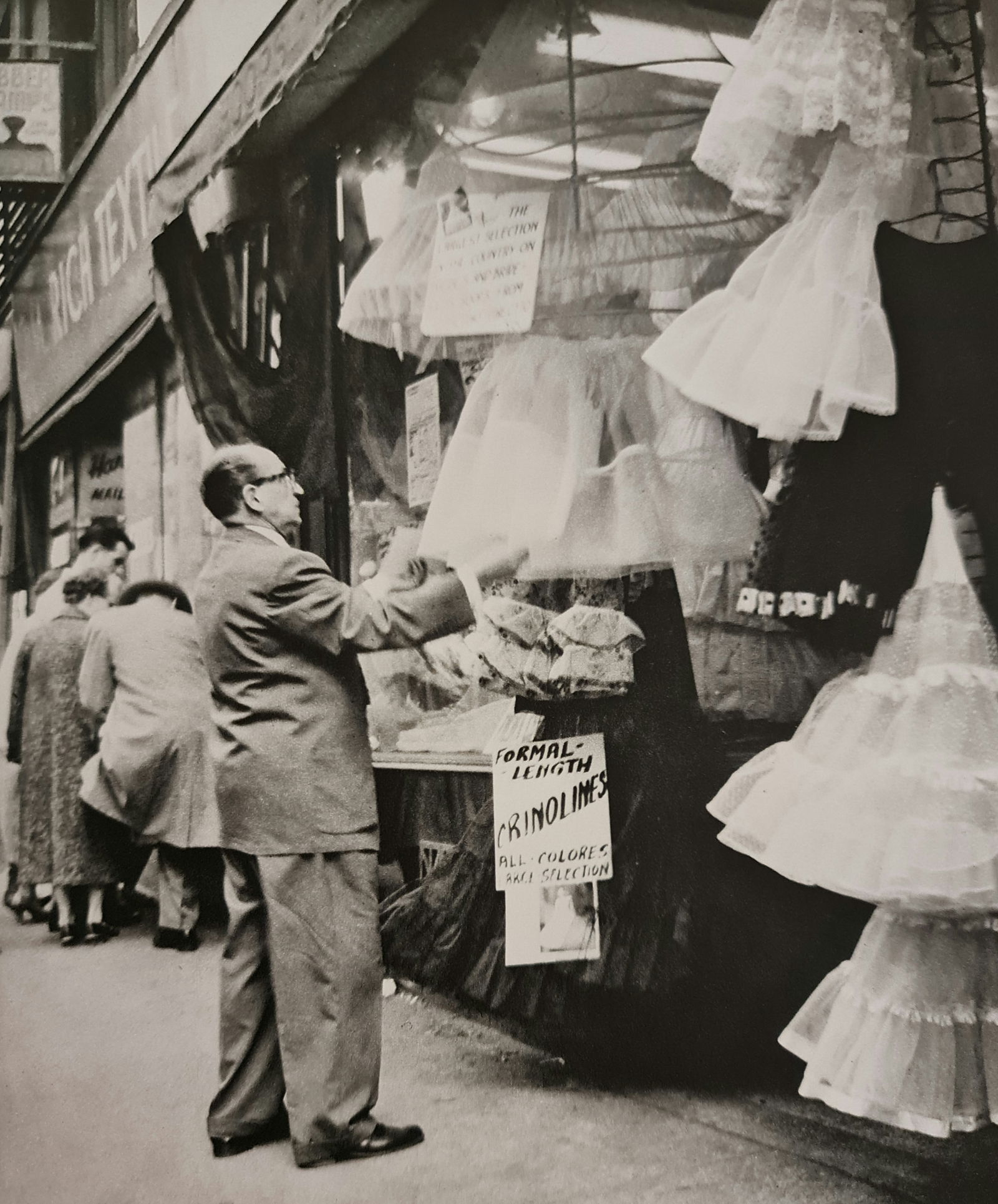 André Kertész, Man looking at dresses, New York, 1957: Photographer: André Kertész, born Andor Kertész, was a Hungarian-born photographer known for his groundbreaking contributions to photographic composition and the photo essay. Subject: Man looking a