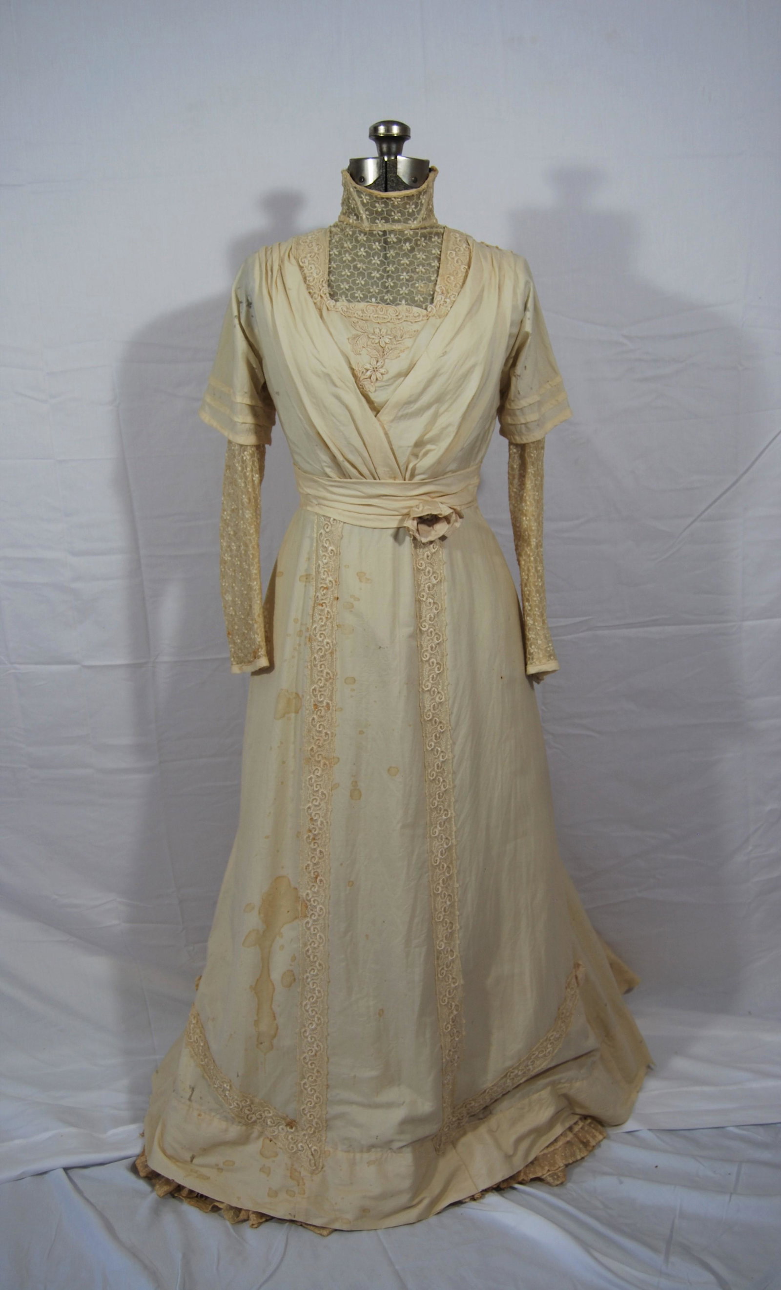 Antique Victorian Era Wedding Dress & Dress Form: Antique Victorian Era Wedding Dress. The full length wedding dress appears to be silk with high lace collar, lace neck insert, lace sleeves, lace applique on the bodice and skirt, 3 rosettes on the fr