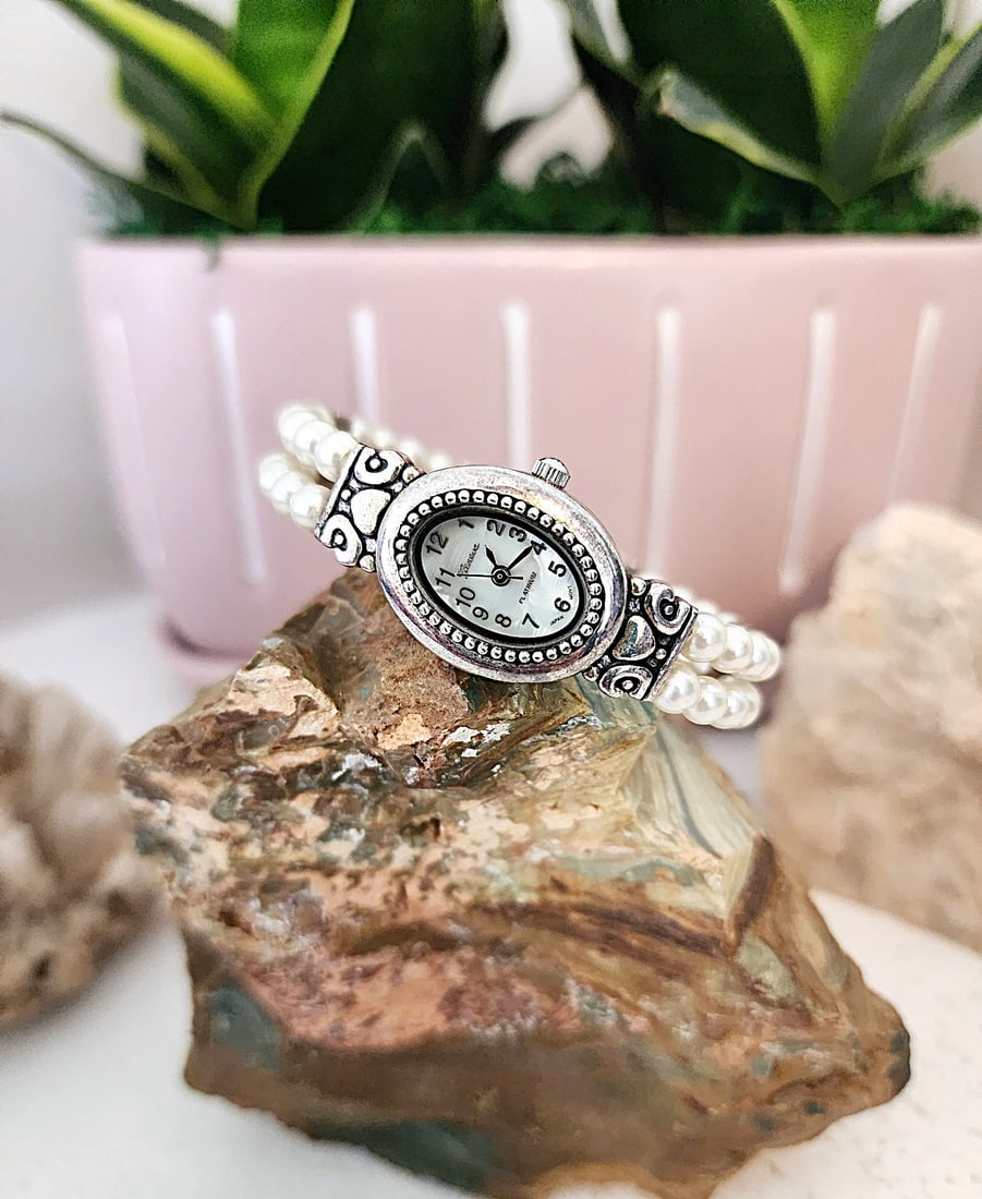 Vintage Geneva Platinum Cuff watch - Pealized Face: This watch features a small oval face with pearlized face and a decorative metal casing. Stainless Steel back. It features a double strand faux pearl cuff band, It is for a smaller wrist - 5 - 6". New