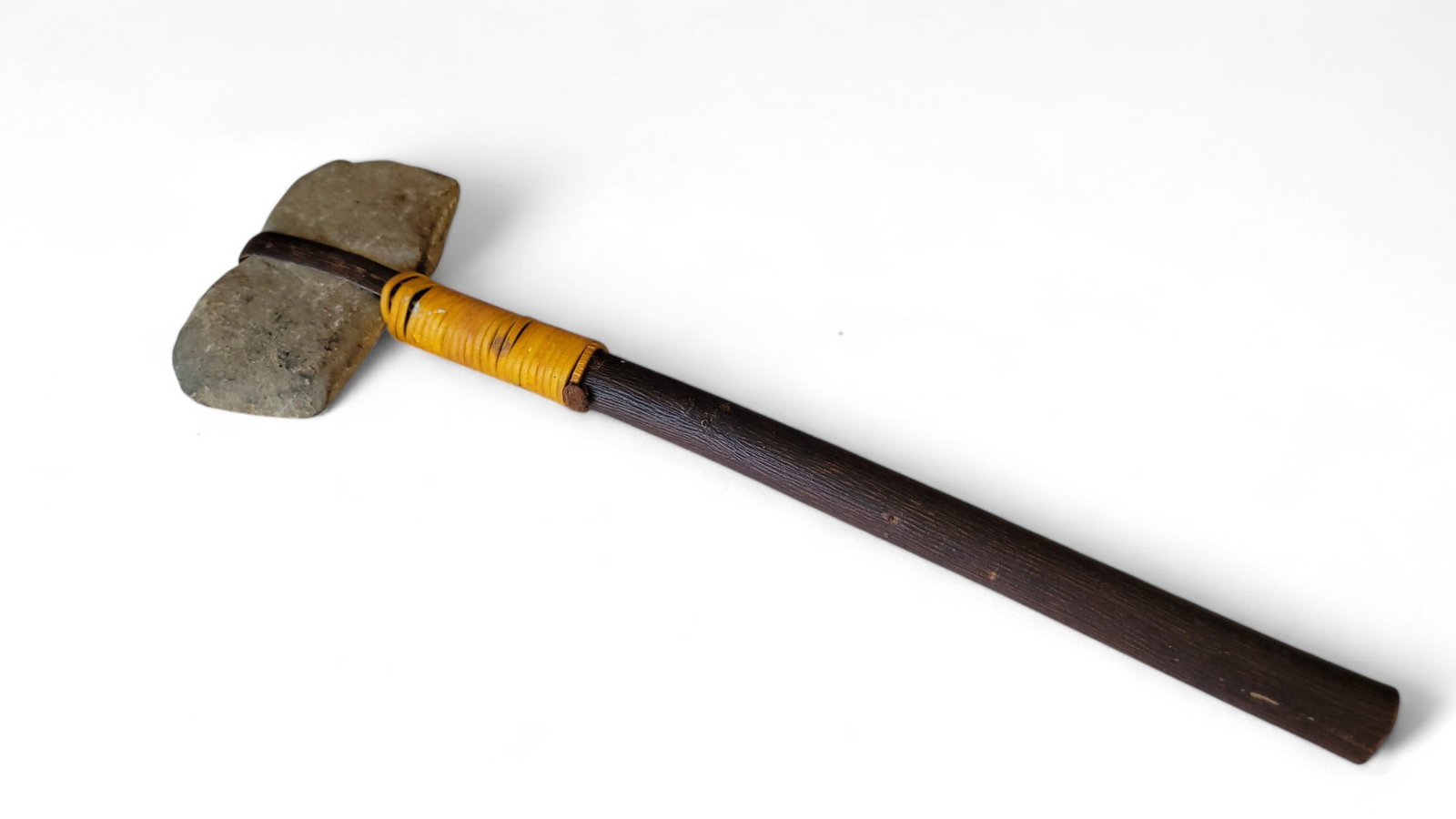 Native American Carved Stone TomaHawk: An evocative artifact of early human ingenuity, this primitive stone axe features a robust dark wooden handle paired with a carefully shaped stone head. The head is securely fastened using a yellow wr