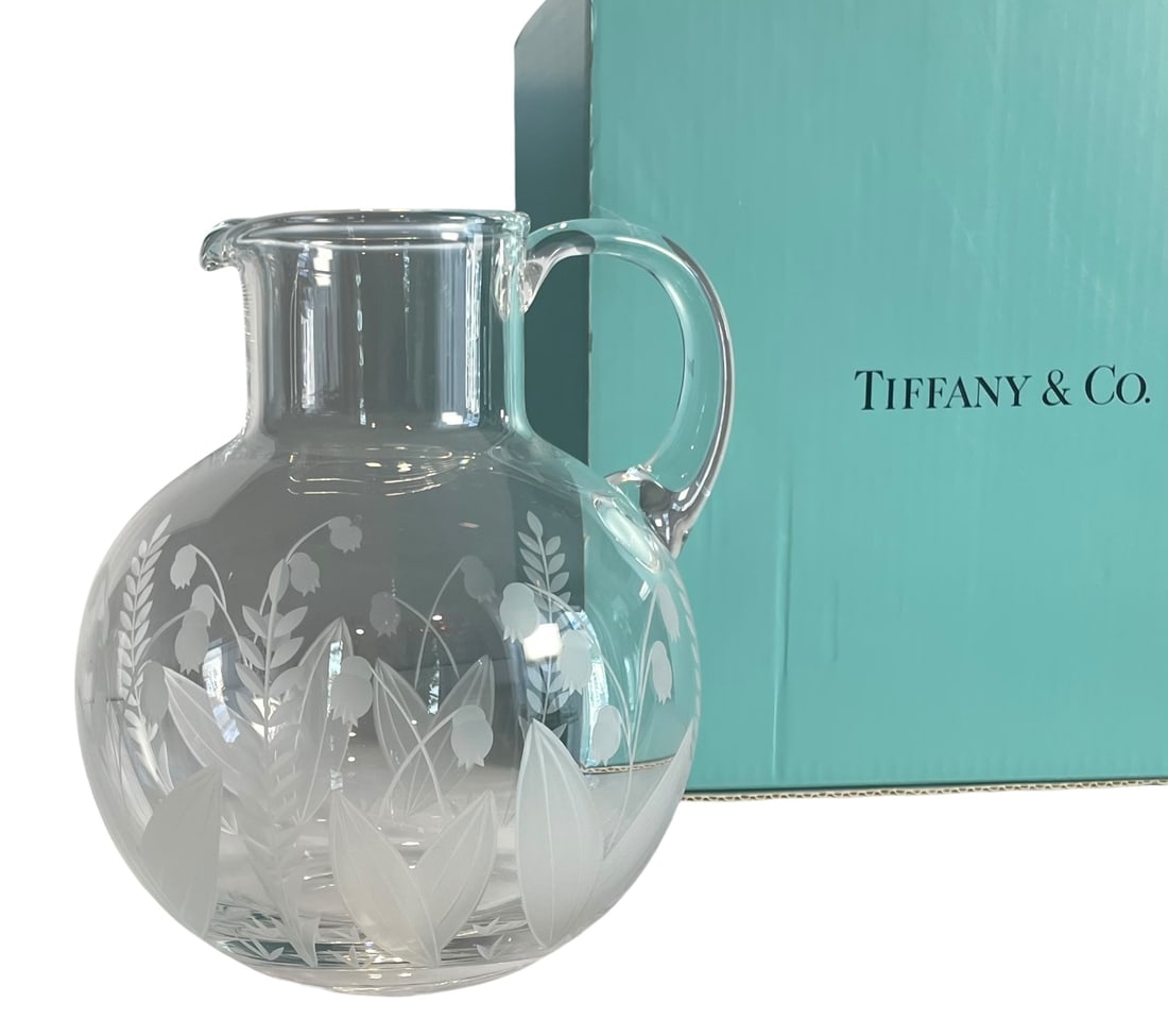 "Lily of the Valley" Glass Pitcher by Tiffany & Co.: "Lily of the Valley" Glass Pitcher by Tiffany & Co. Original box and packaging included. Etched "Lily of the Valley" pattern, and signed Tiffany & Co on the bottom.Pitcher is approx 8.5" tall. Box