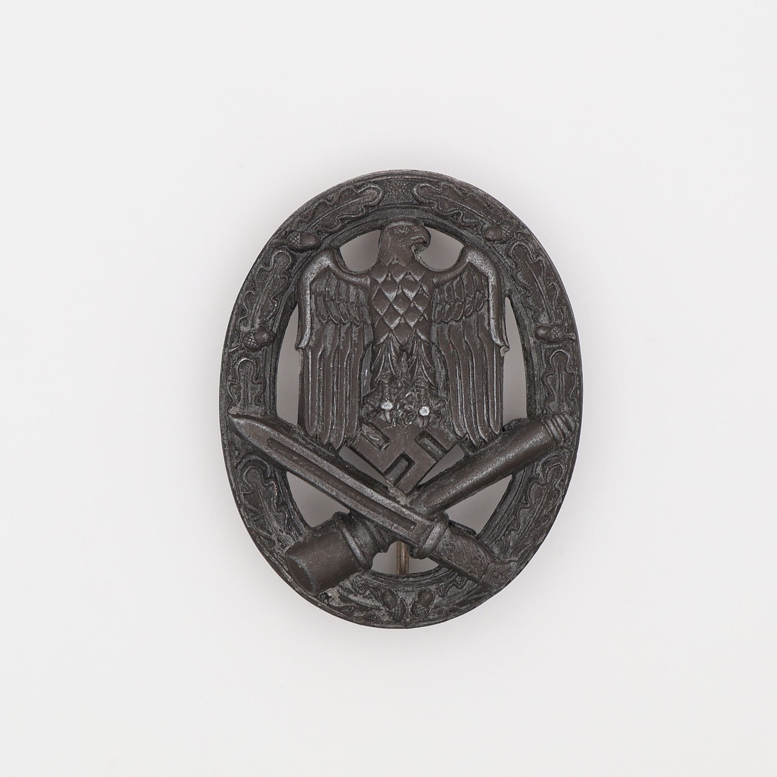 German WWII General Assault Badge: German, Third Reich (c. 1939-1945). General Assault Badge (Allgemeines Sturmabzeichen), in silvered zinc, an oval oak-leaf wreath enclosing an eagle grasping a mobile swastika above a crossed bayonet 